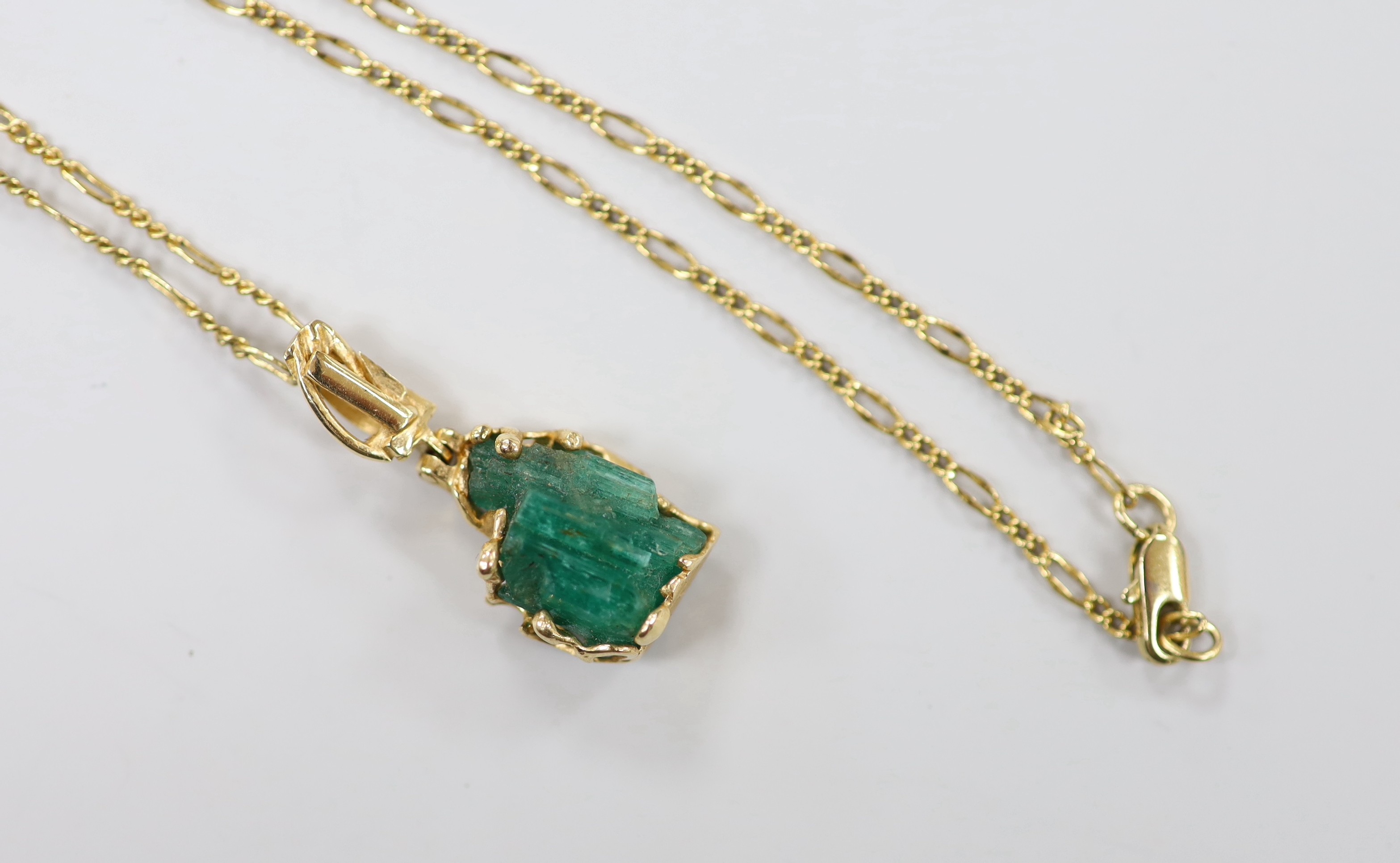 A yellow metal mounted carved emerald boulder set pendant, overall 34mm, gross weight 6 grams, on a gilt metal chain.